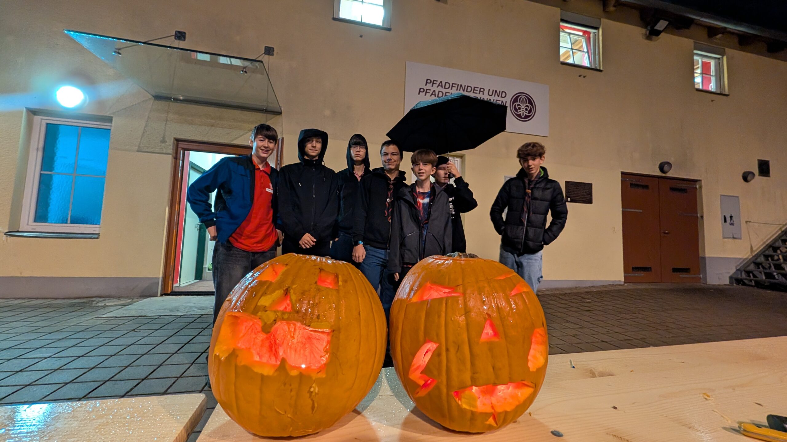 Gruppenfoto der CaEx vor dem Pfadiheim mit zwei beleuchteten, geschnitzten Kürbissen